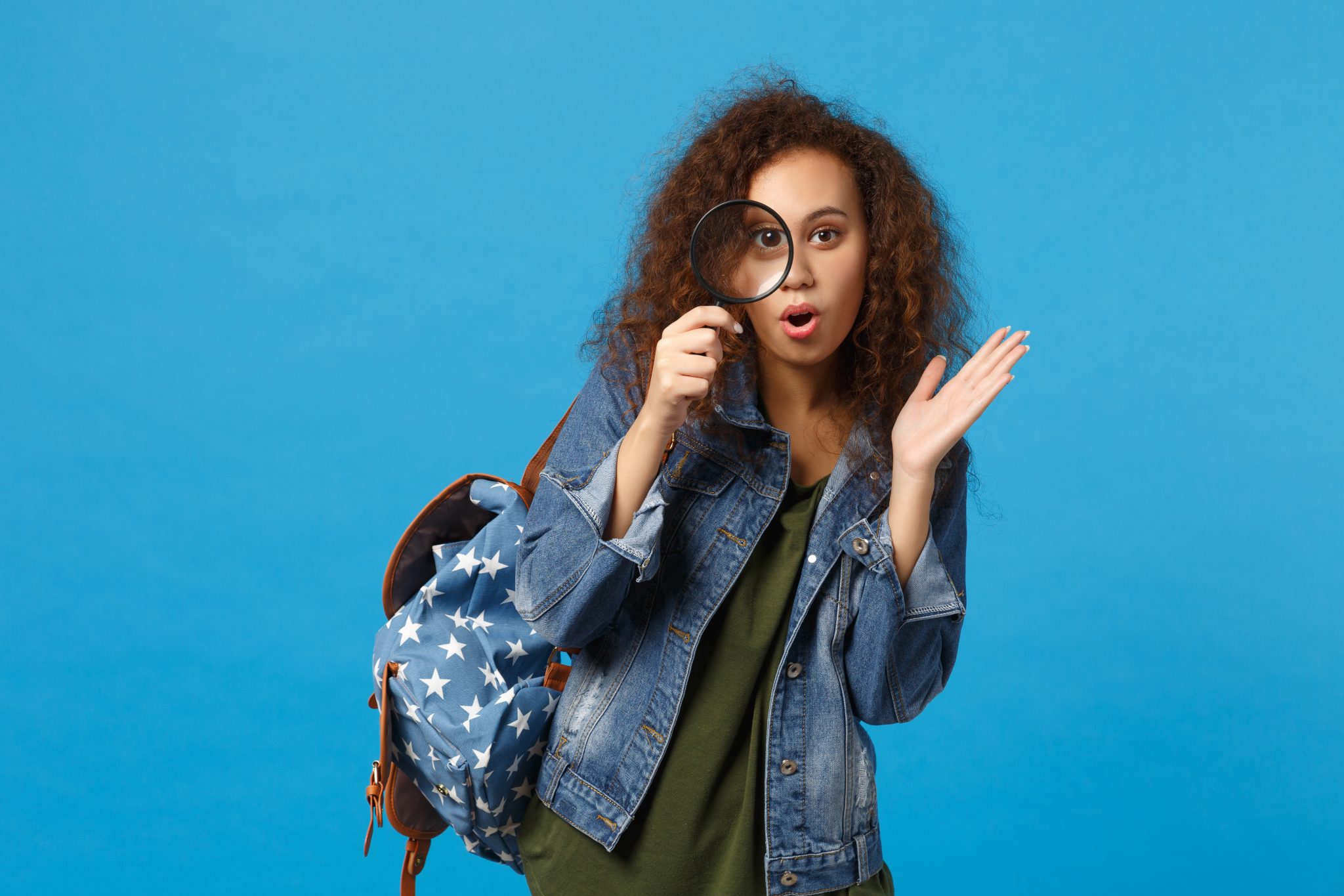 Young african american woman in denim clothes, backpack holding magnifying glass representing being discoverable