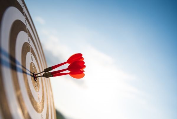 Close up shot red darts arrows in the target center on dark blue sky background. Business target or website design goal concept.