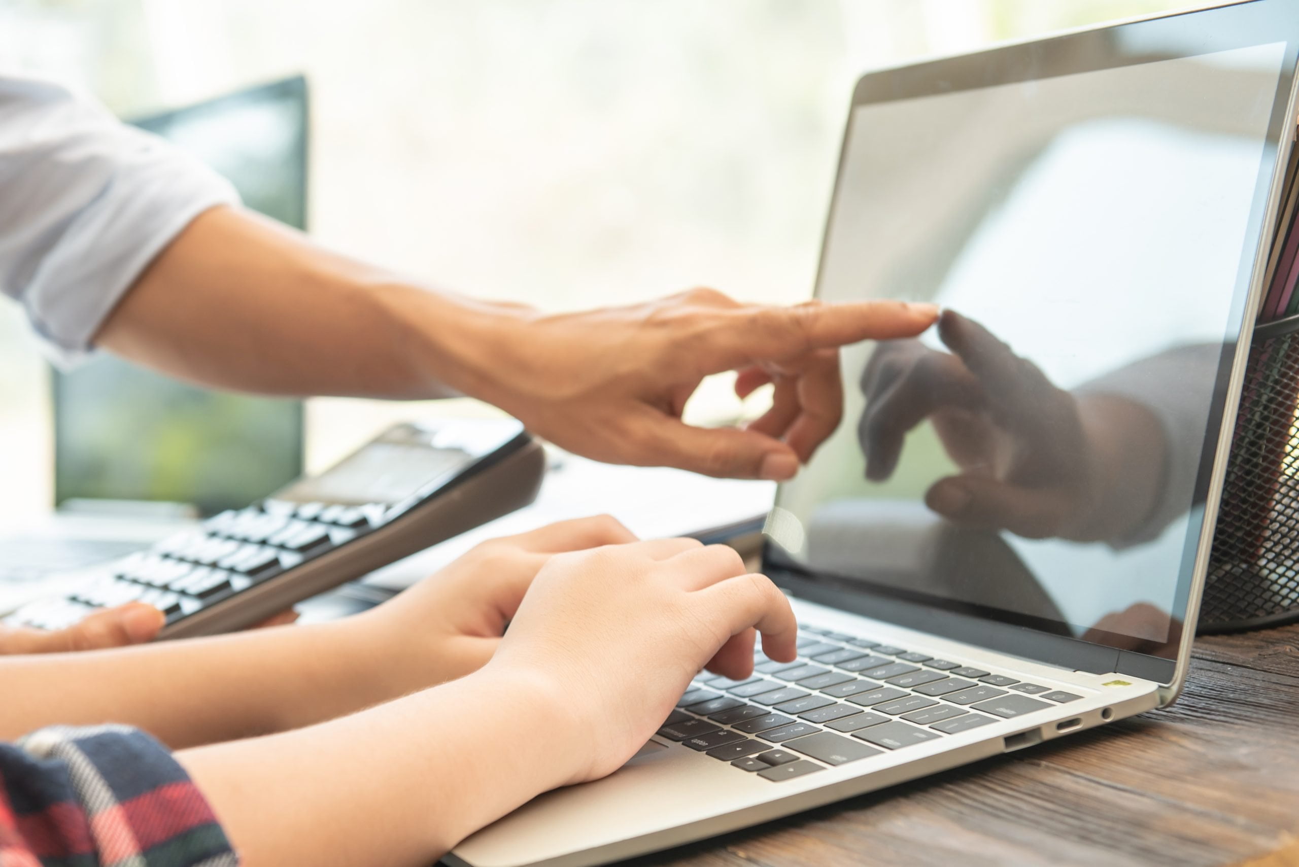 Business woman typing on laptop with colleague pointing at screen while they monitor website activity