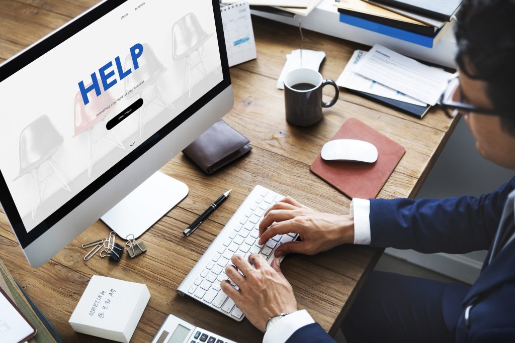 small business man sitting at desktop computer with the word HELP on the screen