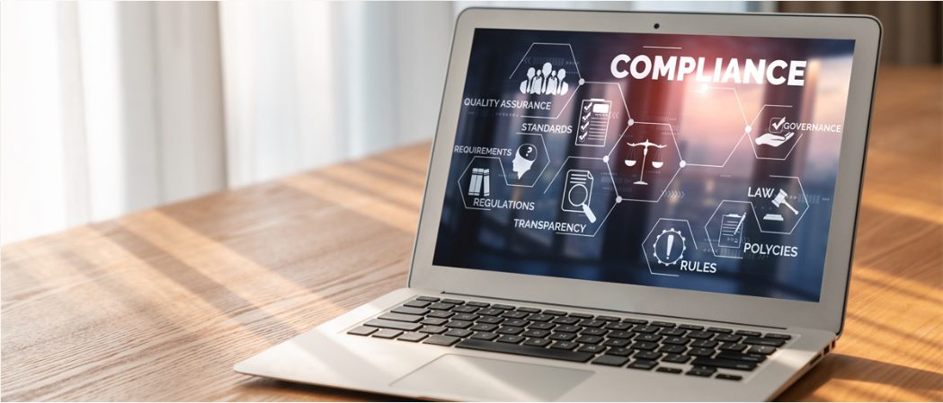 laptop sitting on desk with graphic representation of compliance on the screen